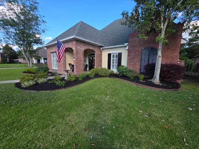 Brick home facade with black mulch landscaping and striped lawn Louisiana