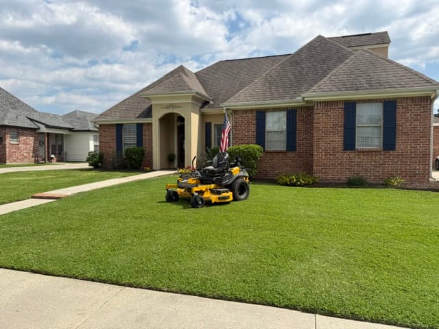 Zero-turn mower in front of brick home with American flag Louisiana