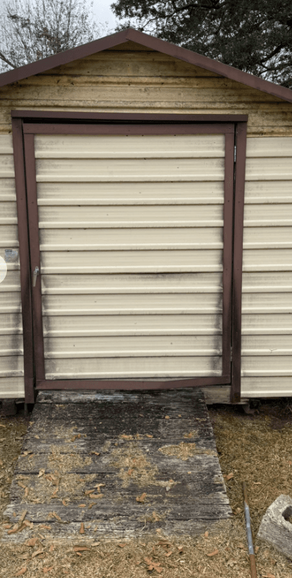 Shed front with mildew-stained siding and weathered ramp before pressure washing